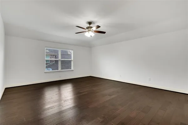 a view of an empty room with wooden floor and a ceiling fan