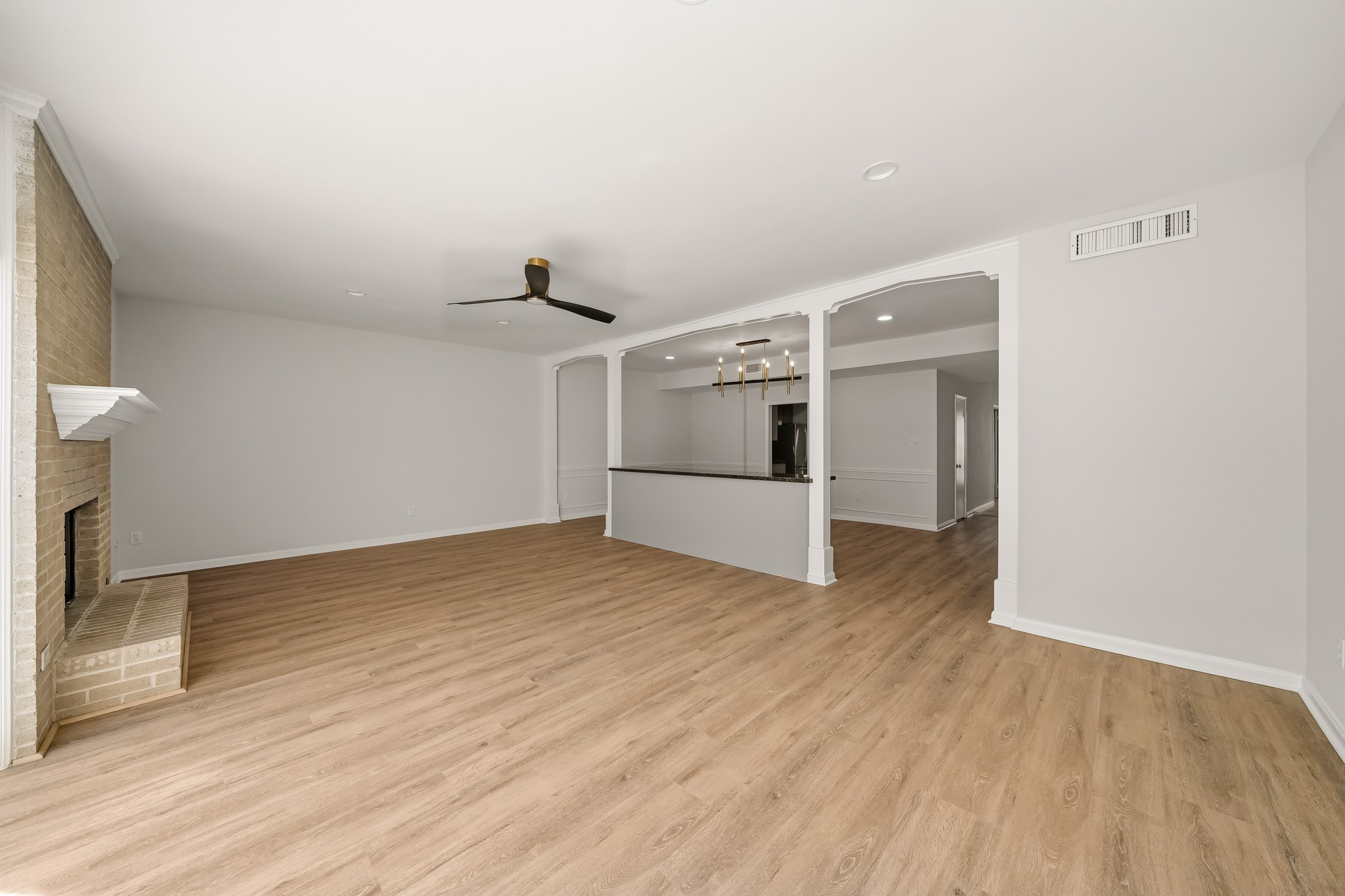 1746 South Gessner Road Houston, TX 77063 - Photo 25 of 25 Open concept living area with elegant wood flooring, modern ceiling fan, and a cozy brick fireplace. The open floor plan seamlessly connects to the dining area and kitchen, enhancing the inviting atmosphere.
