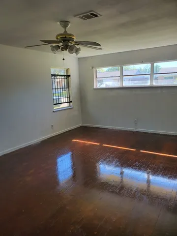 an empty room with wooden floor chandelier fan and windows