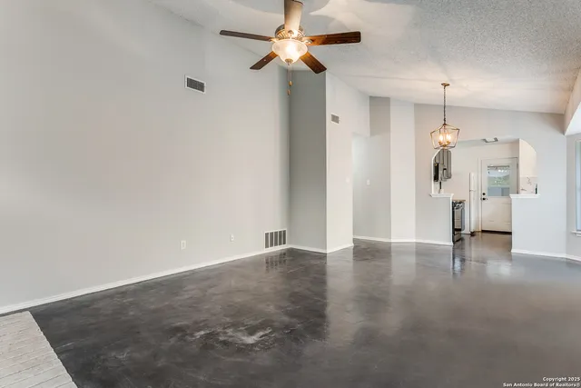 a view of an empty room with wooden floor and a ceiling fan