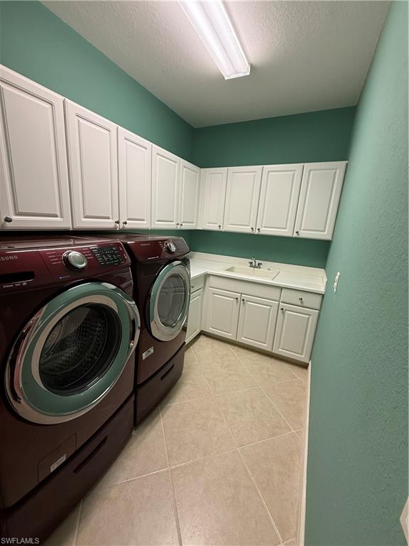 7168 Lemuria Circle, Unit 1701 Naples, FL 34109 - Photo 13 of 30 Laundry area with a textured ceiling, washer and clothes dryer, cabinet space, and light tile patterned floors