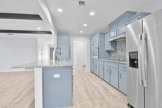 a large kitchen with stainless steel appliances kitchen island granite countertop a refrigerator a sink dishwasher a oven with white cabinets and wooden floor