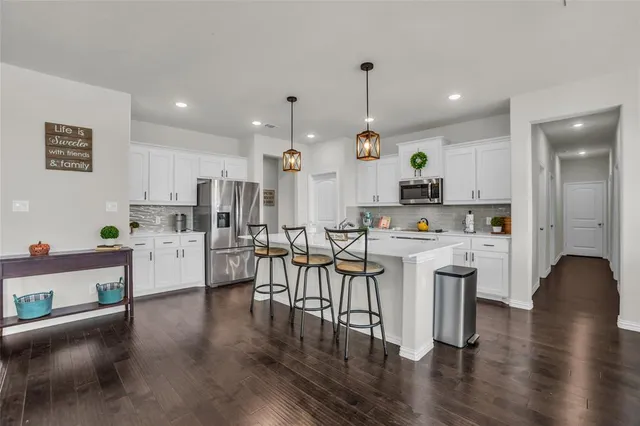 a kitchen with stainless steel appliances granite countertop a refrigerator a stove top oven a sink dishwasher and white cabinets with wooden floor