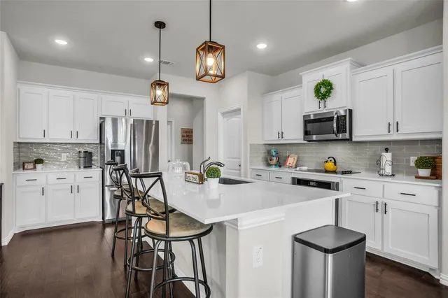 a kitchen with stainless steel appliances a dining table chairs a stove a microwave a sink and white cabinets
