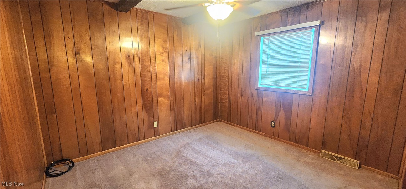 9090 Radcliffe Road Adamsville, OH 43802 - Photo 9 of 19 Spare room featuring carpet flooring, wood walls, and ceiling fan