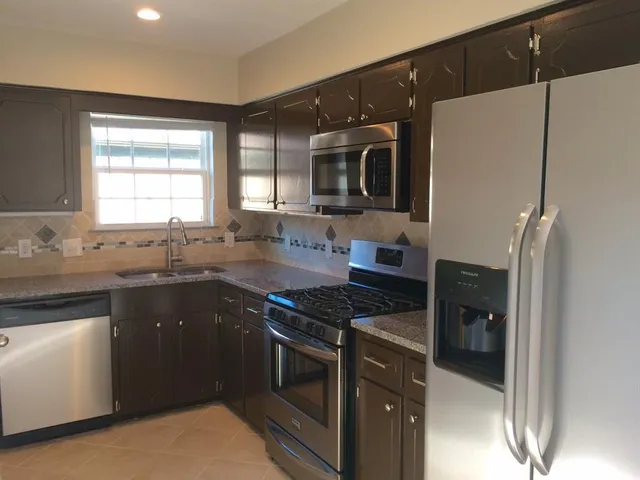 a kitchen with granite countertop a refrigerator stove a sink and dishwasher with wooden floor