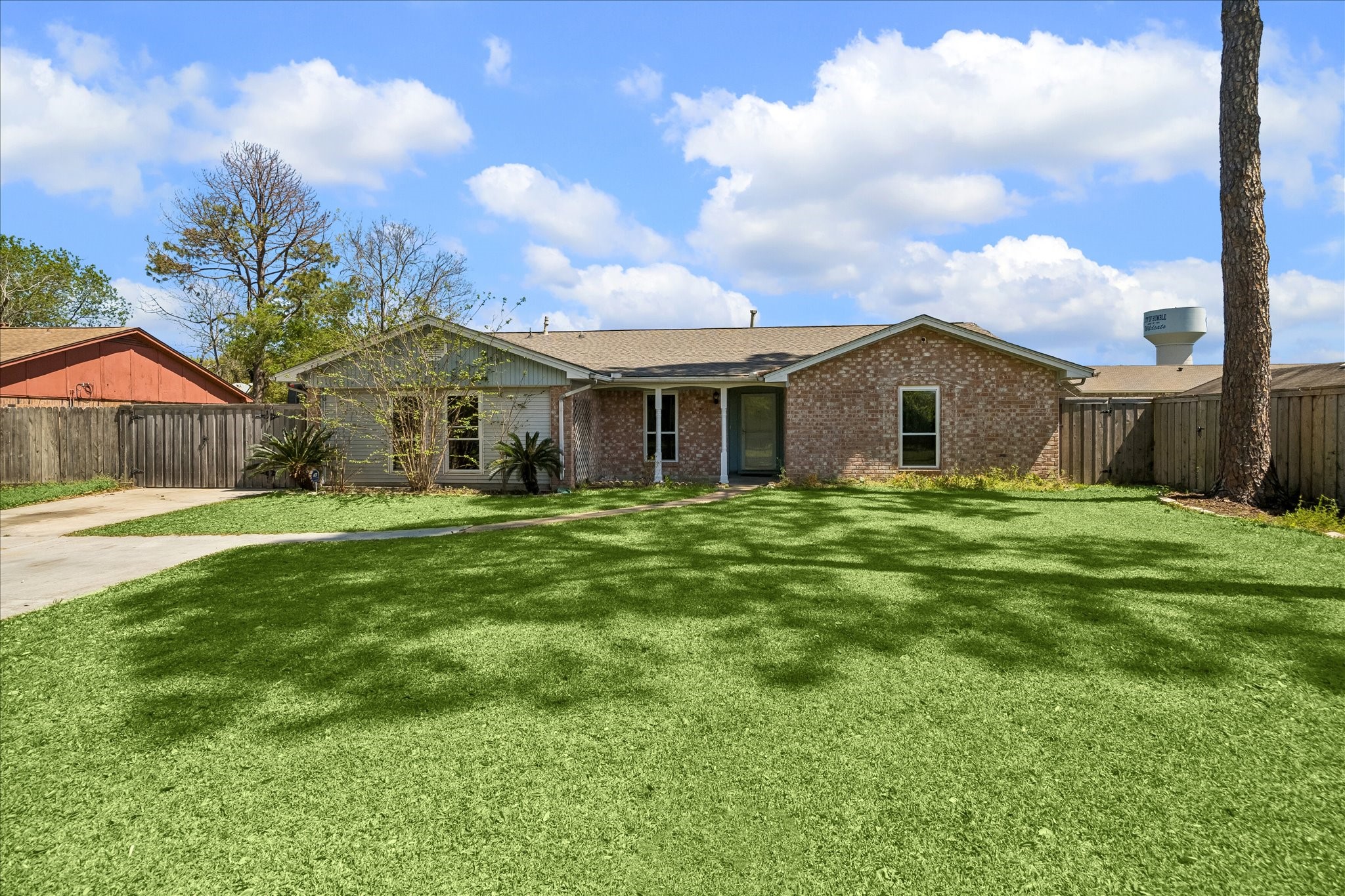 Charming brick home with a spacious front yard, nestled behind a wooden fence for privacy and offering a serene suburban vibe.