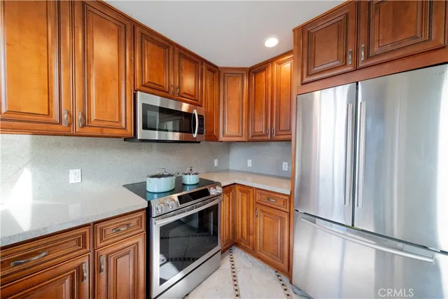 a kitchen with stainless steel appliances granite countertop a refrigerator a stove a sink and dishwasher wooden cabinets with wooden floor