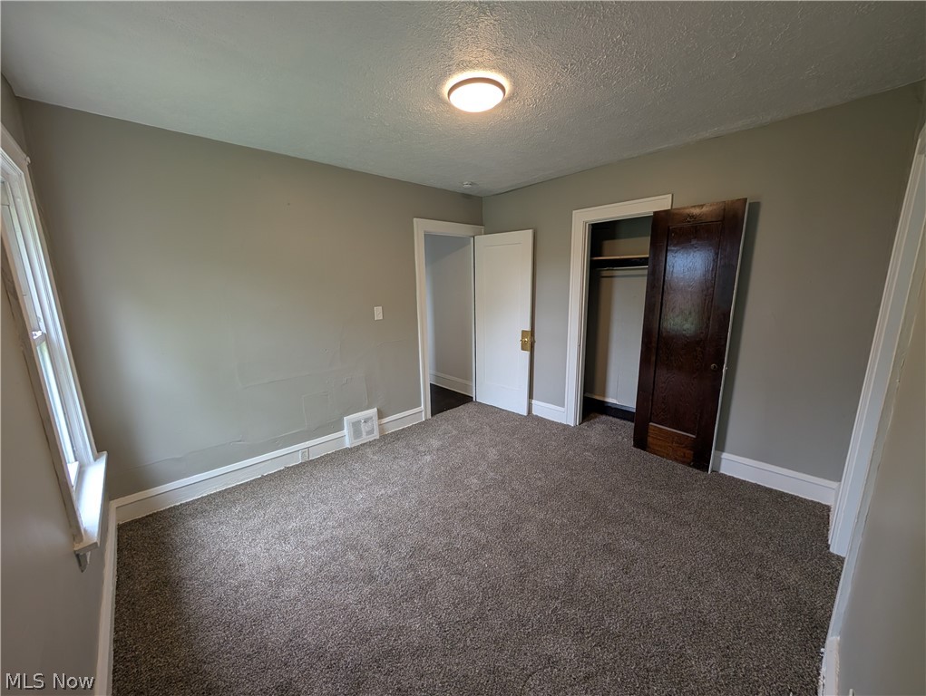 475 East 146th Street Cleveland, OH 44110 - Photo 17 of 28 Carpeted room featuring light gray walls, a window with white trim, a flush mount ceiling light, and an open closet with a dark wood door