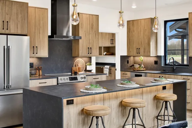 a kitchen with stainless steel appliances granite countertop a refrigerator a sink a stove and chairs with wooden floor