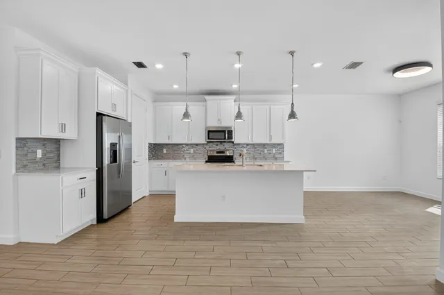 a view of kitchen with stainless steel appliances granite countertop a stove a sink a refrigerator and white cabinets with wooden floor