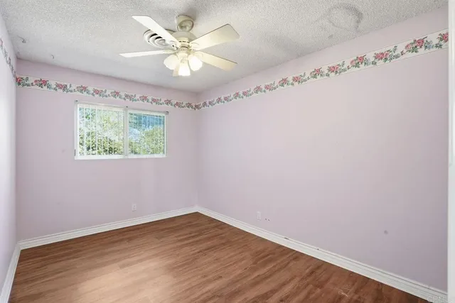 an empty room with wooden floor fan and windows