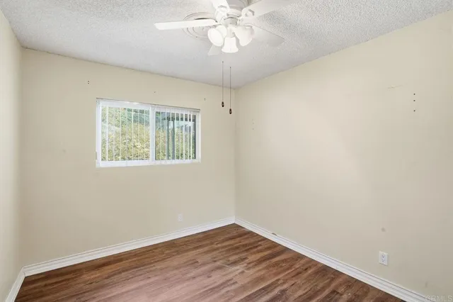an empty room with wooden floor chandelier fan and windows