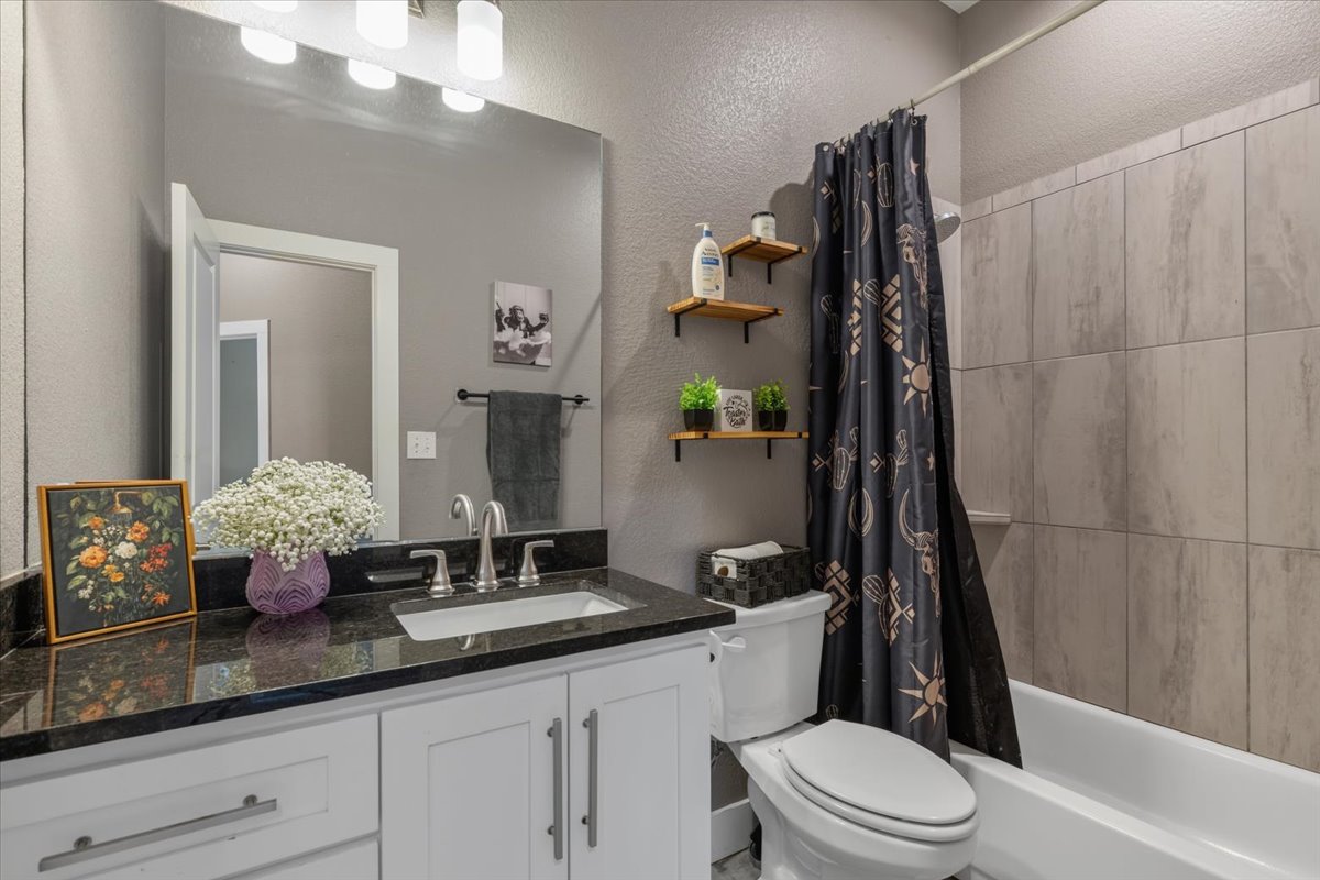 145 Cardinal Loop Paige, TX 78659 - Photo 19 of 40 A well-appointed bath features a dark granite countertop and a tiled shower-tub combination.