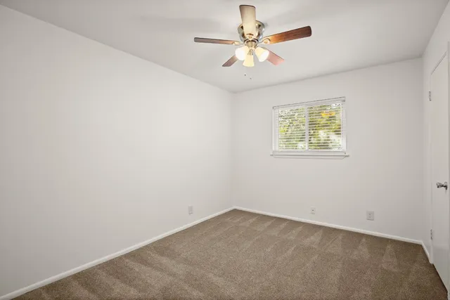 an empty room with a chandelier fan and windows