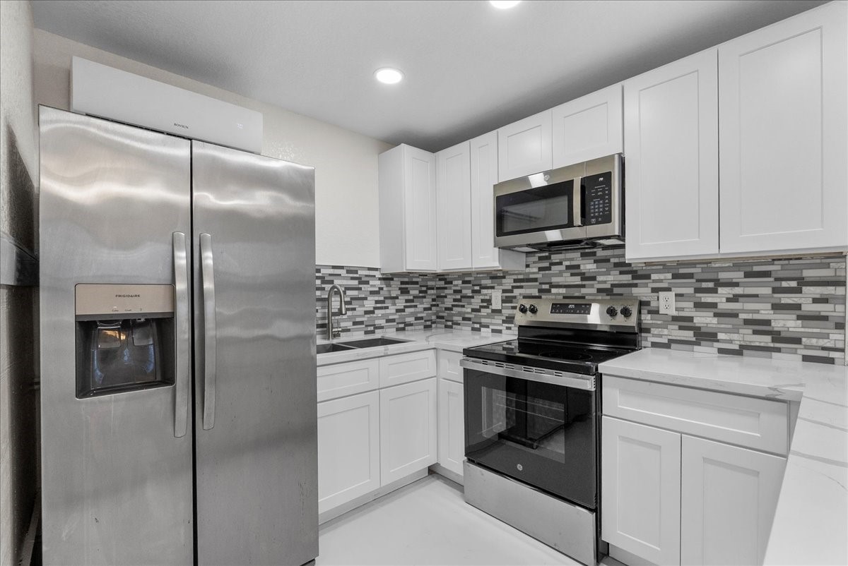 515 Thunder Road Surfside Beach, TX 77541 - Photo 11 of 31 Modern kitchen with stainless steel appliances, white cabinetry, and a stylish tile backsplash.