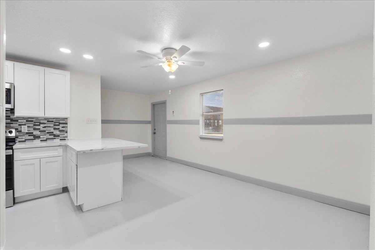 515 Thunder Road Surfside Beach, TX 77541 - Photo 13 of 31 This bright, open kitchen features modern white cabinetry, a stylish tile backsplash, and recessed lighting. The room includes a ceiling fan and a window for natural light, creating a welcoming atmosphere.