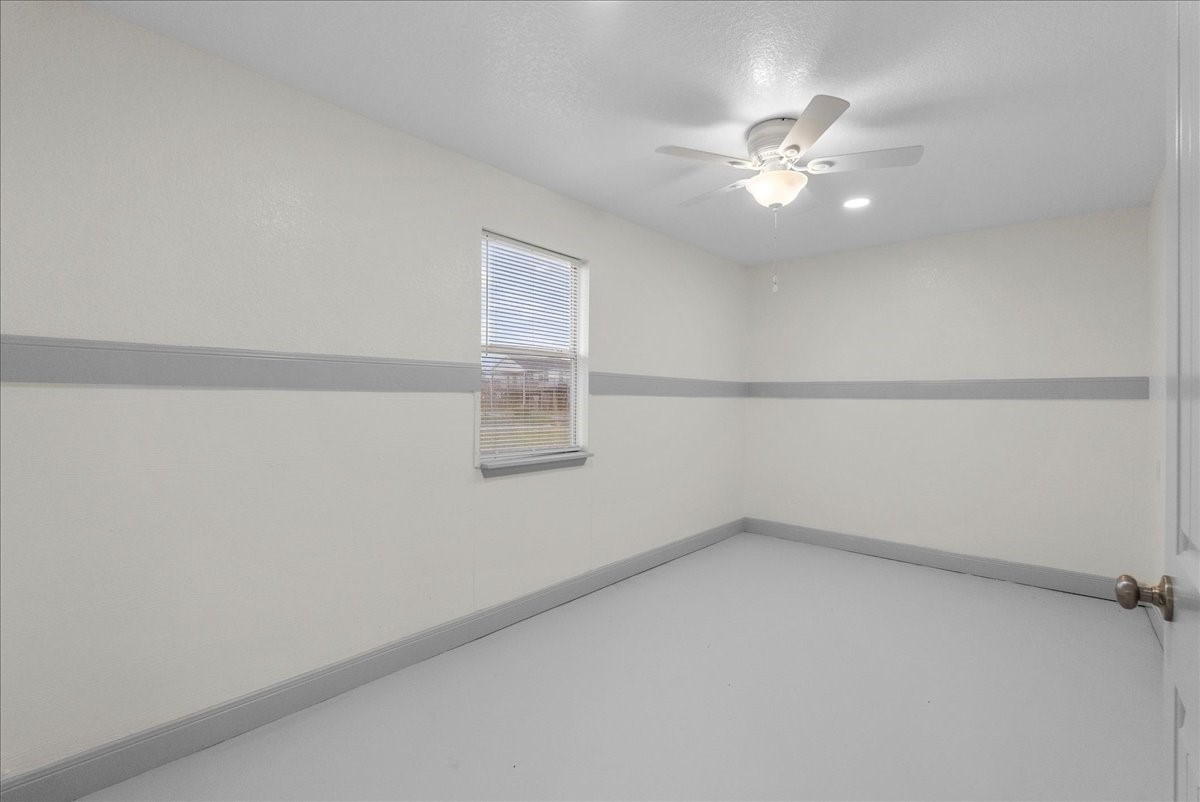 515 Thunder Road Surfside Beach, TX 77541 - Photo 15 of 31 Bright, neutral-toned room with a ceiling fan and single window, featuring a gray accent stripe and baseboards. Ideal for a bedroom or home office.