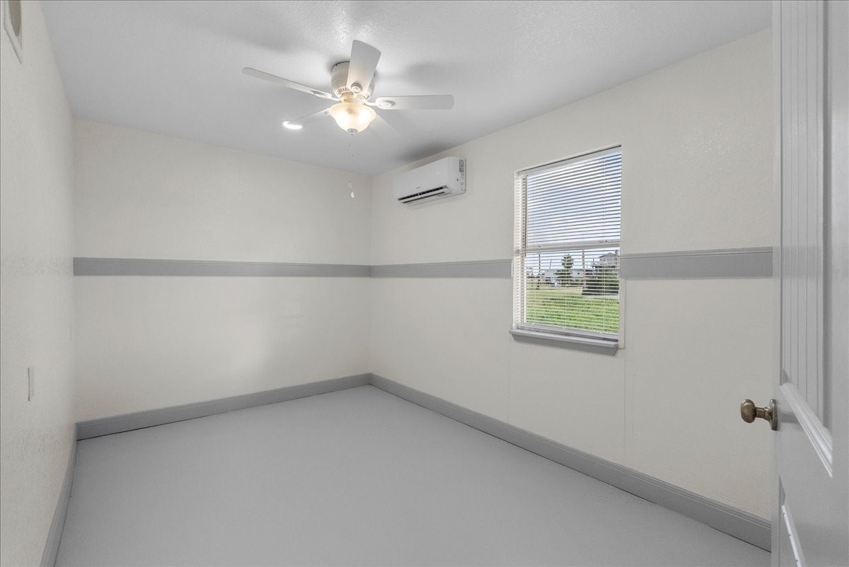 515 Thunder Road Surfside Beach, TX 77541 - Photo 17 of 31 This room features a neutral color palette with a ceiling fan and a wall-mounted air conditioning unit. It has a window allowing natural light and a view of the outdoors, making it a simple, functional space.