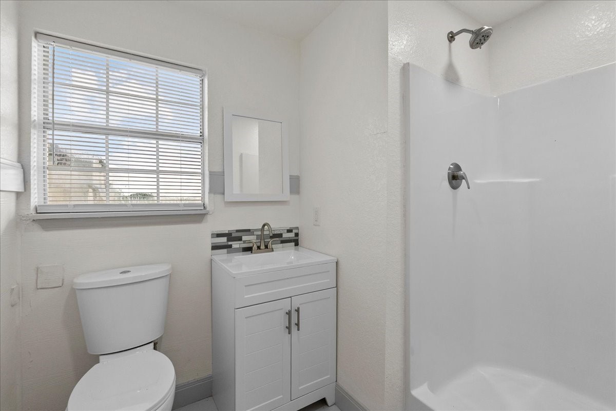 515 Thunder Road Surfside Beach, TX 77541 - Photo 20 of 31 This is a bright, modern bathroom featuring a walk-in shower, a toilet, and a sleek vanity with a mirror. The room has a large window allowing natural light to fill the space.