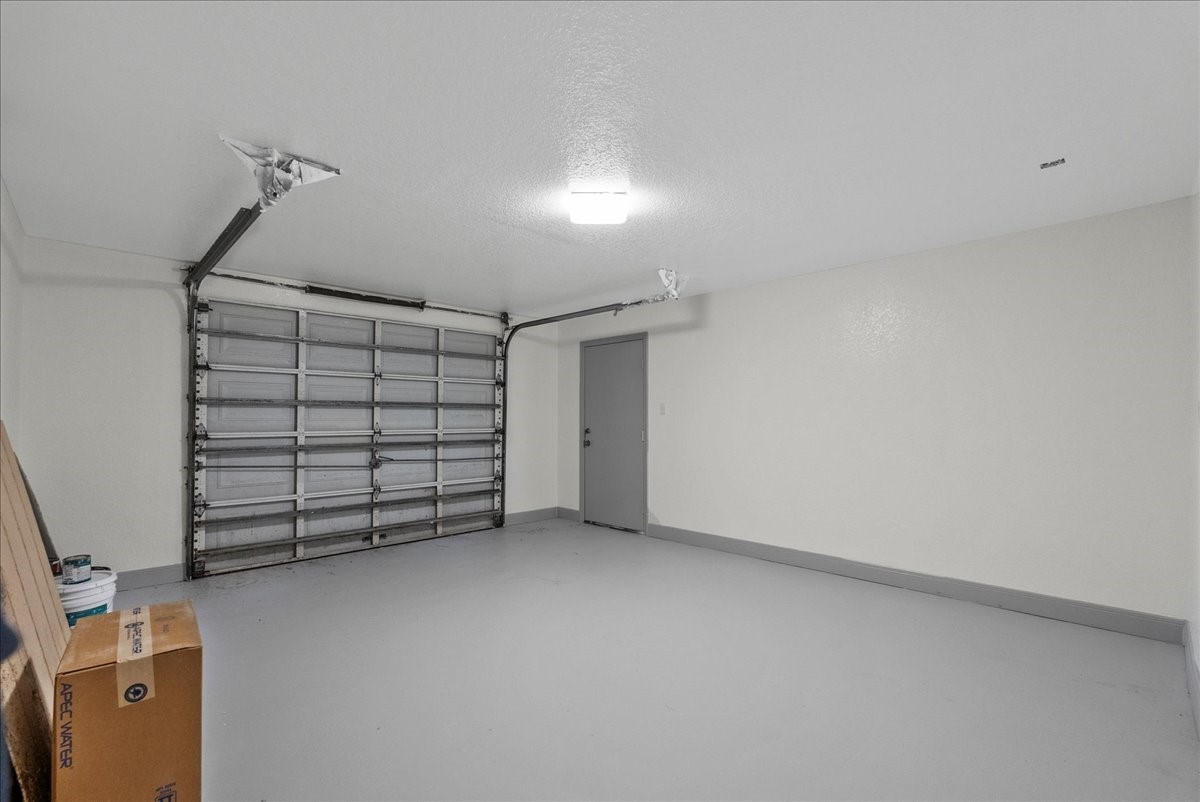 515 Thunder Road Surfside Beach, TX 77541 - Photo 26 of 31 This photo shows a clean, spacious garage with a single overhead door, neutral-colored walls, and a gray concrete floor. It's well-lit and includes a side entry door, offering ample space for storage or parking.