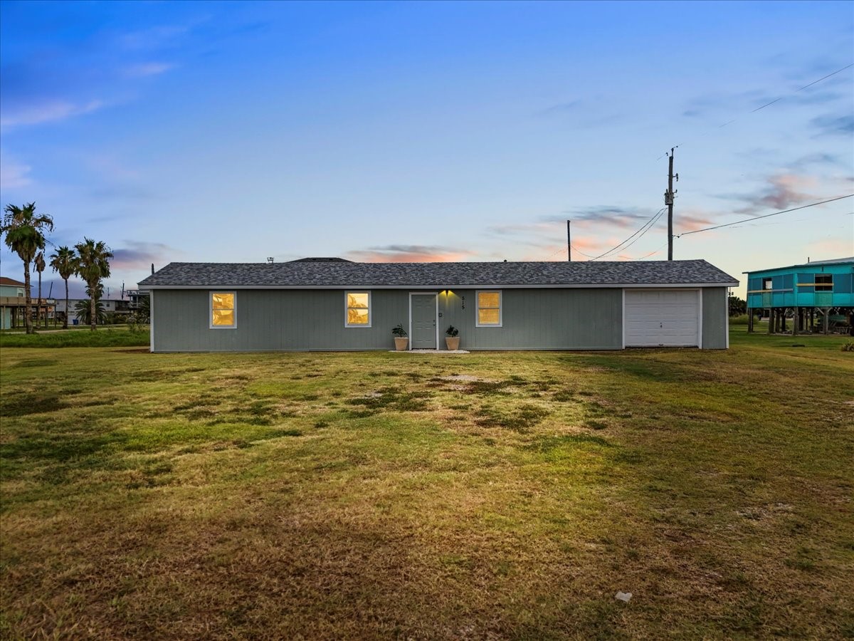 515 Thunder Road Surfside Beach, TX 77541 - Photo 27 of 31 This photo shows a single-story, ranch-style home with a light exterior and a spacious front yard. The house features a simple design with a garage on one side, set against a backdrop of a serene evening sky.
