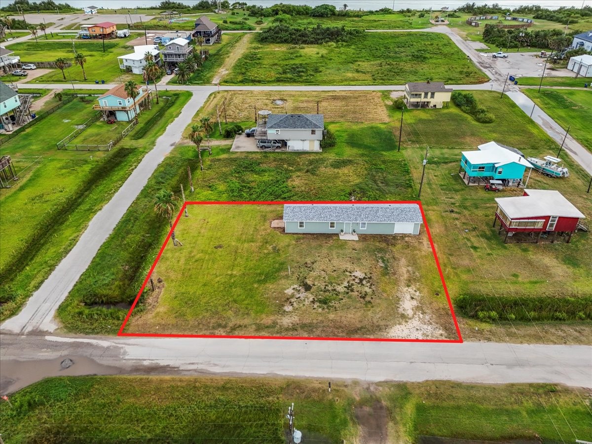 515 Thunder Road Surfside Beach, TX 77541 - Photo 29 of 31 This photo shows a single-story home on a spacious lot, outlined in red, in a quiet, green neighborhood. The property is surrounded by open land and a few neighboring houses, with a view of a water body in the distance, suggesting a peaceful, coastal setting.