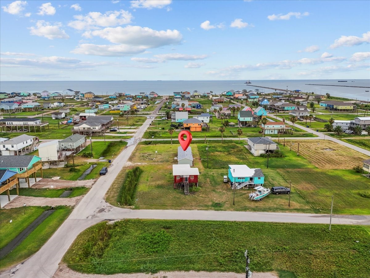 515 Thunder Road Surfside Beach, TX 77541 - Photo 31 of 31 This photo captures a coastal neighborhood with colorful homes, highlighting a specific property marked by a red pin. The area is open and green, with a view of the ocean in the background, suggesting a serene and scenic location.