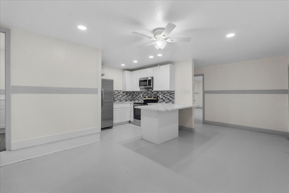 515 Thunder Road Surfside Beach, TX 77541 - Photo 6 of 31 This photo shows a bright, modern kitchen with white cabinetry, stainless steel appliances, and a stylish tiled backsplash. The open layout includes a ceiling fan and recessed lighting, creating a welcoming space for cooking and entertaining.