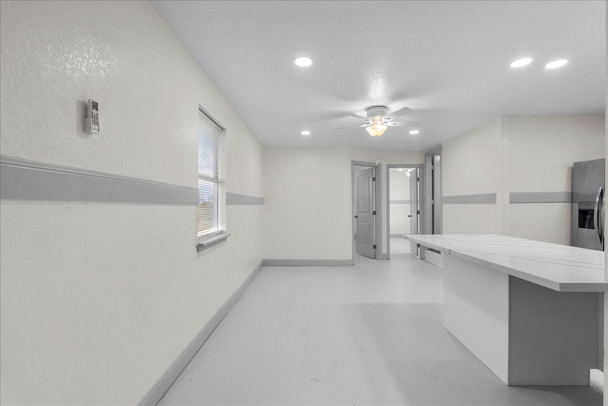 515 Thunder Road Surfside Beach, TX 77541 - Photo 8 of 31 Bright, spacious kitchen with modern fixtures, featuring a ceiling fan, ample lighting, and a large countertop. The room has neutral tones and leads to additional spaces through open doorways.