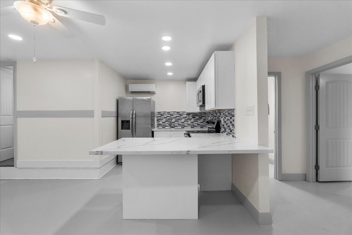 515 Thunder Road Surfside Beach, TX 77541 - Photo 9 of 31 This photo showcases a modern kitchen with sleek white cabinetry and countertops, a stylish mosaic tile backsplash, and stainless steel appliances. The space is well-lit with recessed lighting and features a ceiling fan, providing a bright and airy atmosphere.