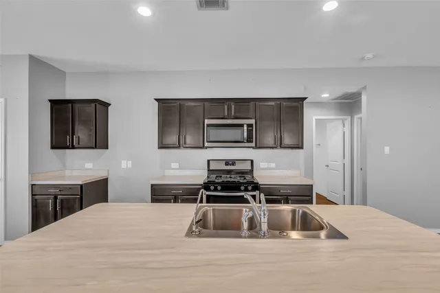 a large kitchen with a large counter top a sink stainless steel appliances and cabinets