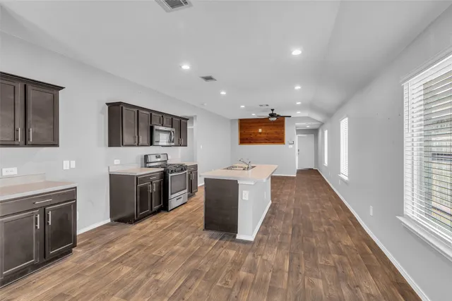 a large kitchen with stainless steel appliances a large counter top a stove a sink a refrigerator and a window