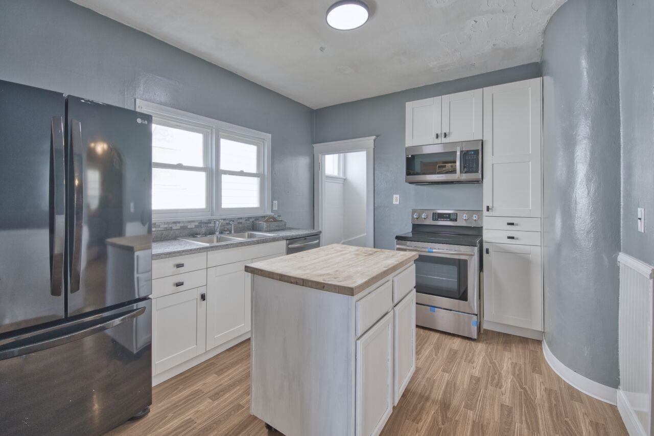 25 3rd Street Southwest Chisholm, MN 55719 - Photo 11 of 44 Kitchen featuring butcher block countertops, appliances with stainless steel finishes, white cabinetry, radiator heating unit, and light wood-style flooring