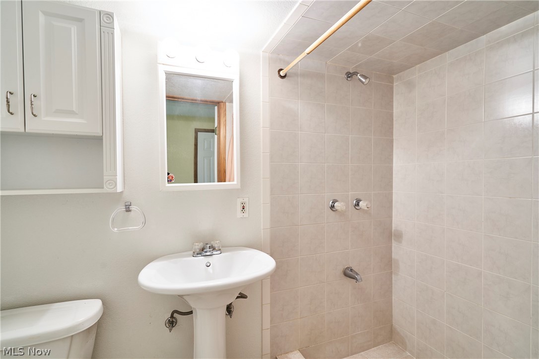 1963 Haines Road Madison, OH 44057 - Photo 23 of 34 Bathroom featuring a pedestal sink, wall- mounted medicine cabinet, and tiled shower surround with a fixed shower head