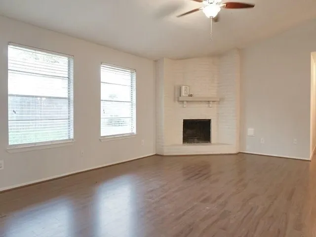 an empty room with wooden floor fireplace and windows