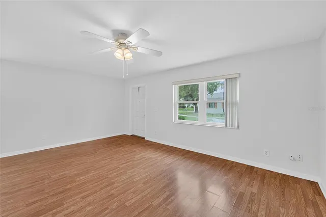 a view of an empty room with chandelier fan and wooden floor