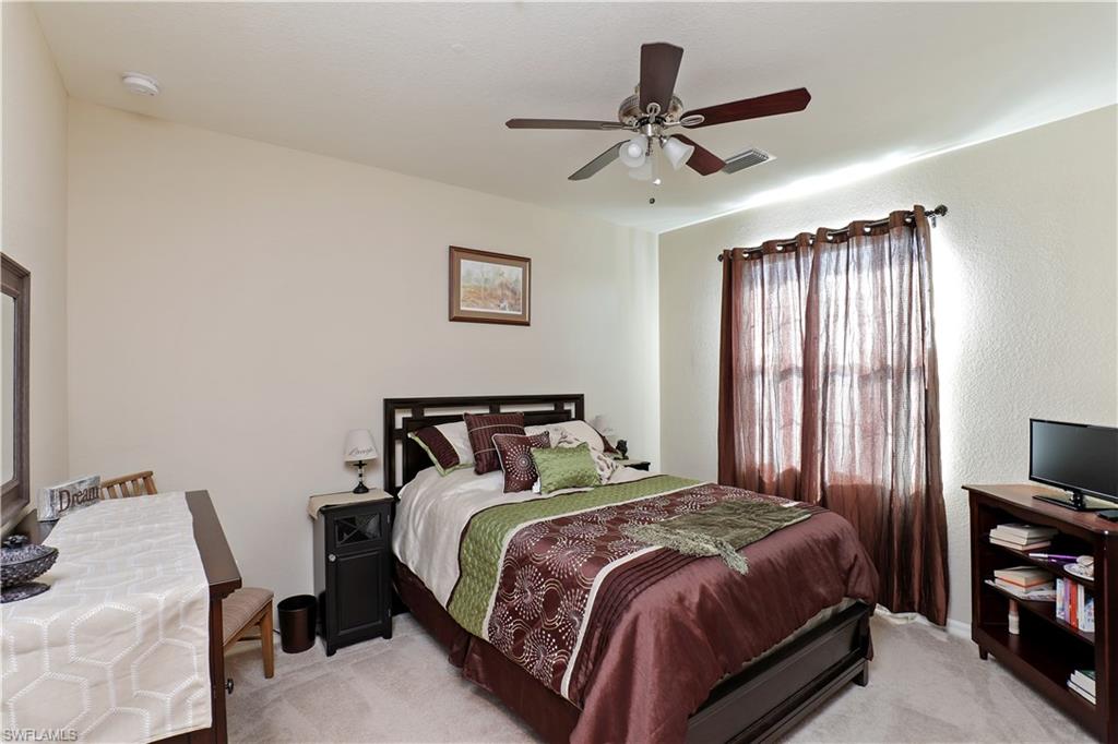 9051 Capistrano Street North, Unit 4308 Naples, FL 34113 - Photo 11 of 20 a bedroom with a bed a ceiling fan and a flat tv screen on the dresser