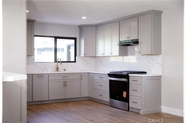 a kitchen with stainless steel appliances granite countertop white cabinets a stove a sink and dishwasher with wooden floor