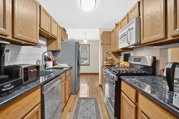 a kitchen with stainless steel appliances granite countertop a stove top oven a refrigerator a sink and dishwasher with wooden floor