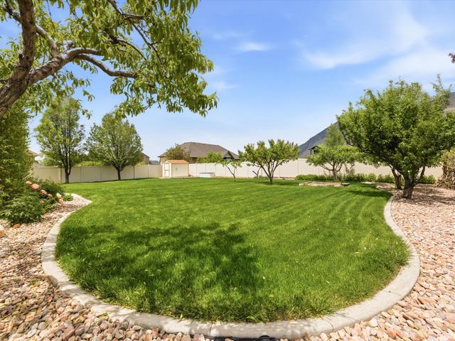 255 East 1200 North Mapleton, UT 84664 - Photo 29 of 37 Expansive backyard featuring a lush lawn, mature trees, decorative rock landscaping, a white privacy fence, and an exterior storage shed