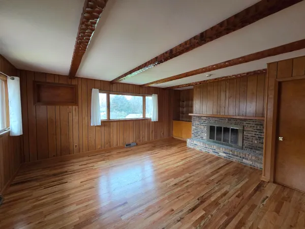 an empty room with wooden floor fireplace and windows