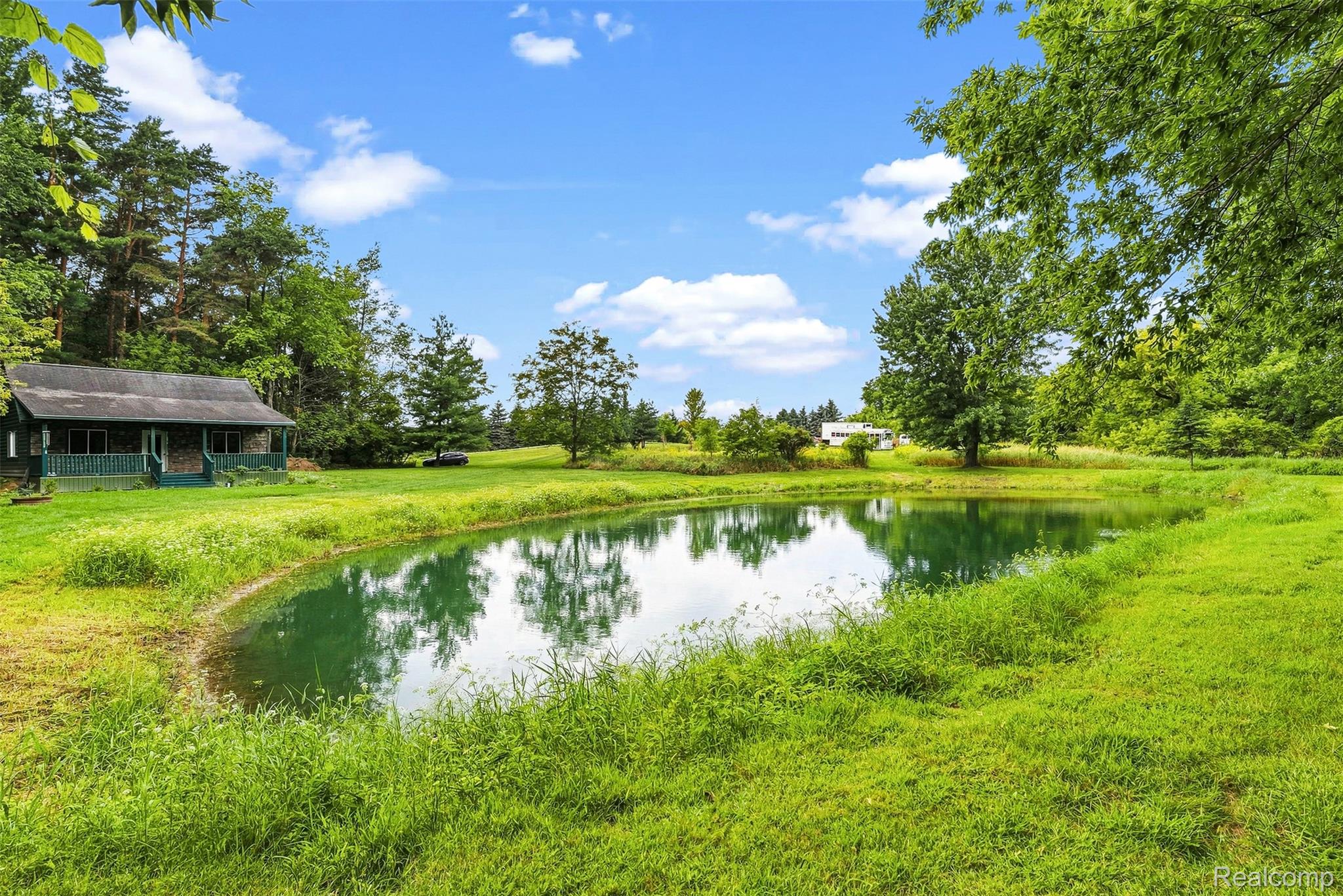 2971 Huron Line Road Cass City, MI 48726 - Photo 49 of 63 Expansive green landscape featuring a tranquil pond, mature trees, and a distant cabin with a covered porch