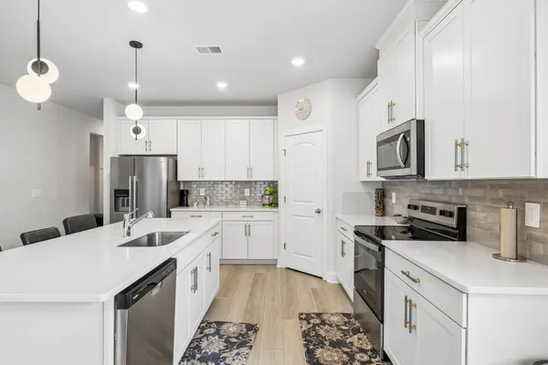 a kitchen that has a lot of white cabinets and stainless steel appliances