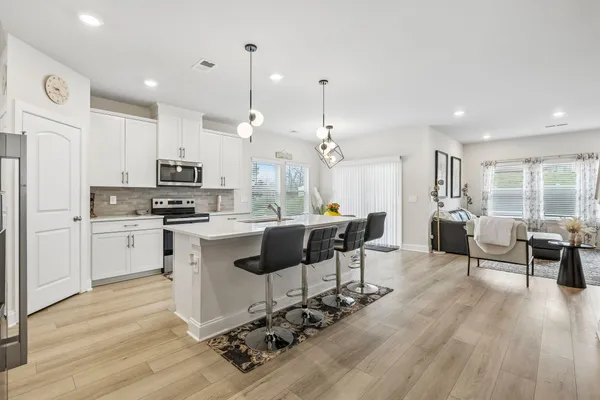 a large white kitchen with lots of counter space dining table and stainless steel appliances