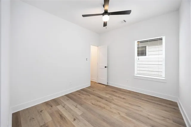 an empty room with wooden floor ceiling fan and windows