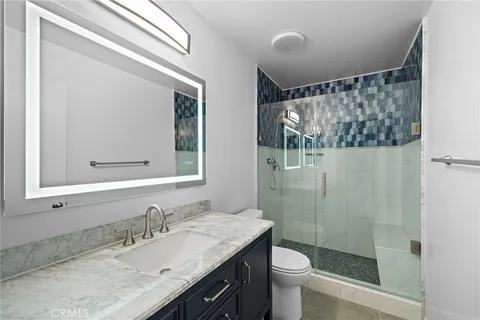 a bathroom with a granite countertop sink a toilet a mirror a vanity and shower