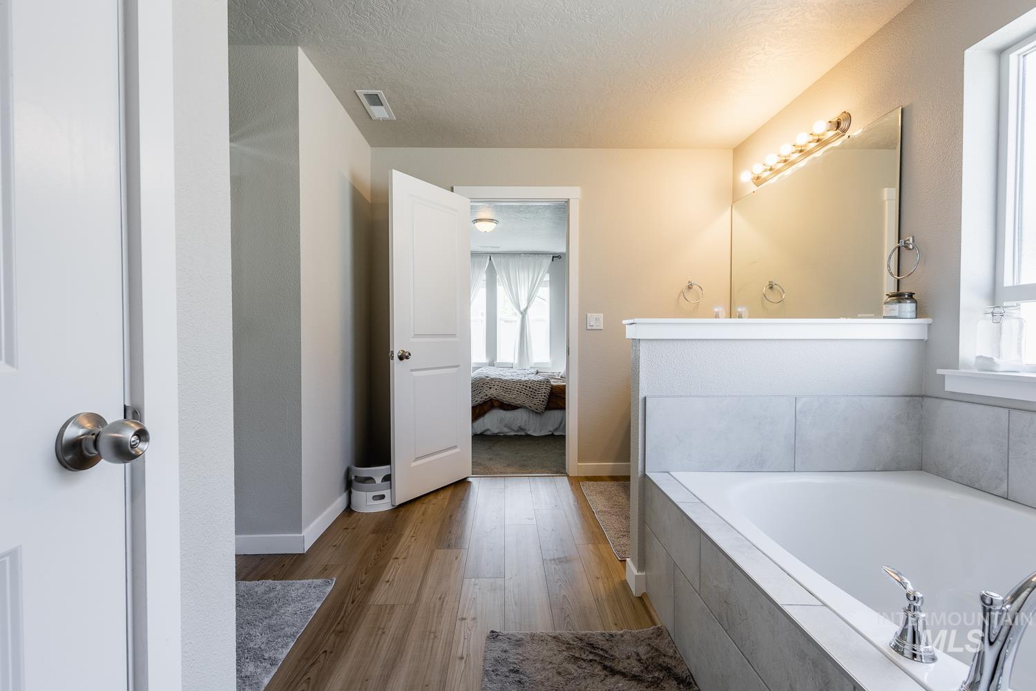 12623 Shadow Peak Street Caldwell, ID 83607 - Photo 32 of 50 Bathroom featuring a built-in soaking tub with light gray tile surround, wood-finish flooring, and a window providing natural light