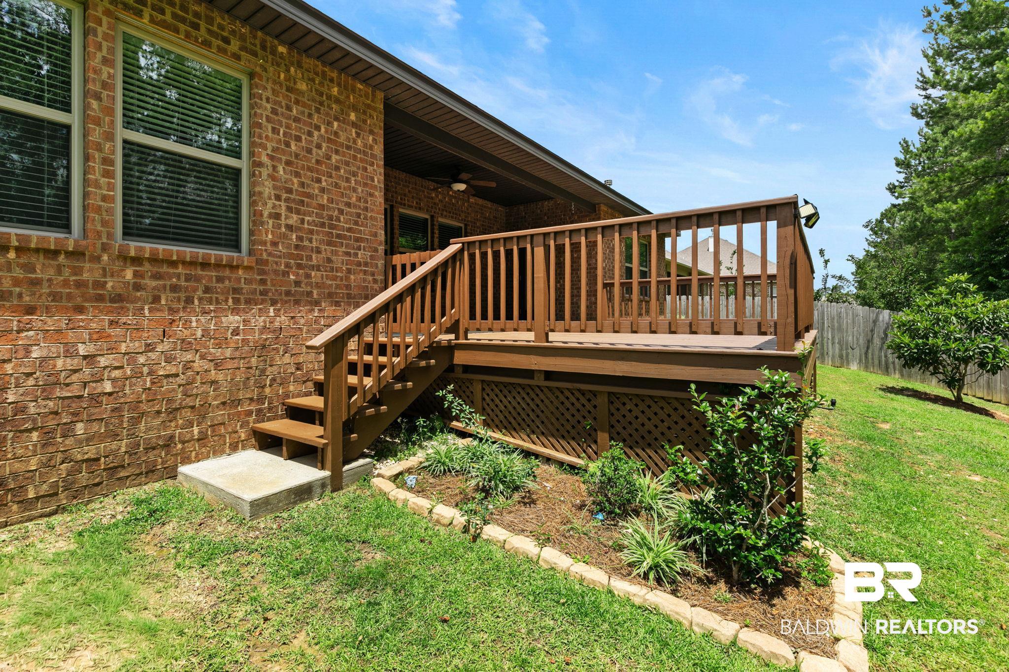 31350 Hoot Owl Road Daphne, AL 36527 - Photo 47 of 94 Brick exterior with a wood-finish deck and railings, featuring a covered patio, staircase access, and a latticework skirt