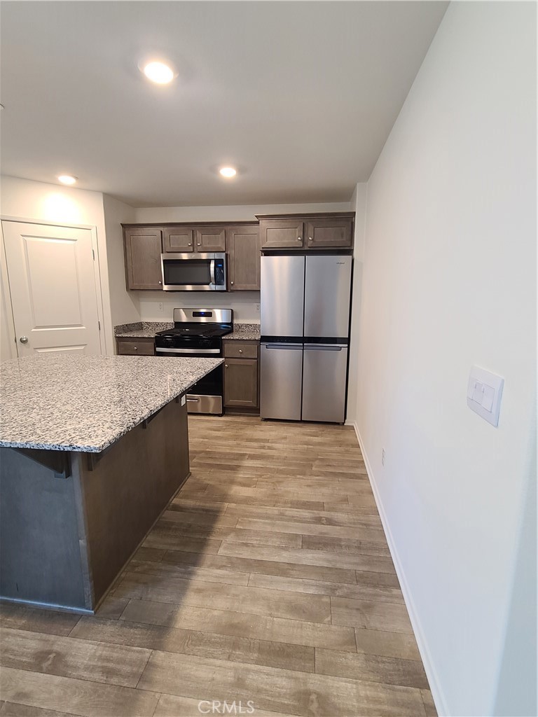 30540 Altima Court Winchester, CA 92596 - Photo 4 of 21 a large kitchen with kitchen island a sink dishwasher a refrigerator and a stove top oven with wooden floor